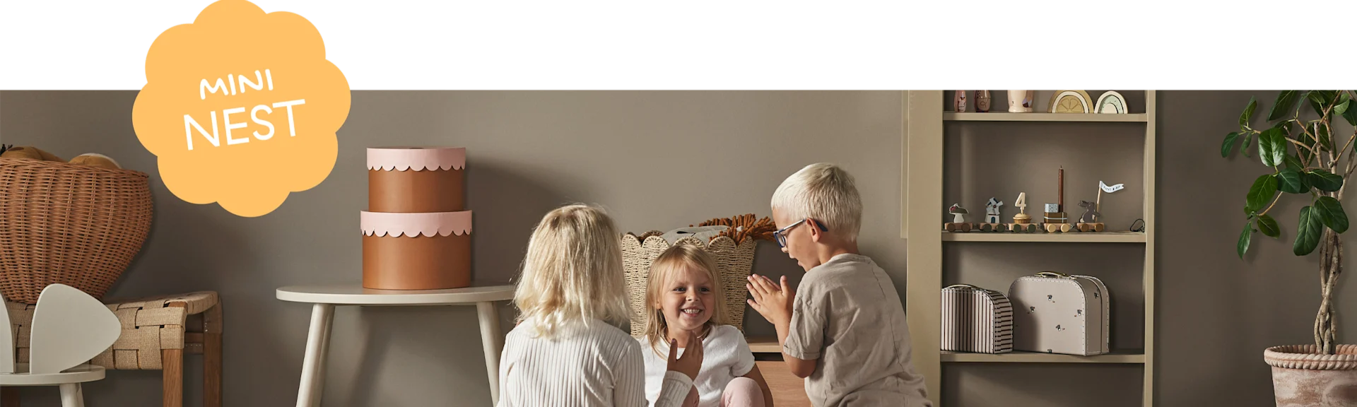 Three children playing in a kids room with a toy train, decorative boxes, and a 'MINI NEST' graphic overlay.