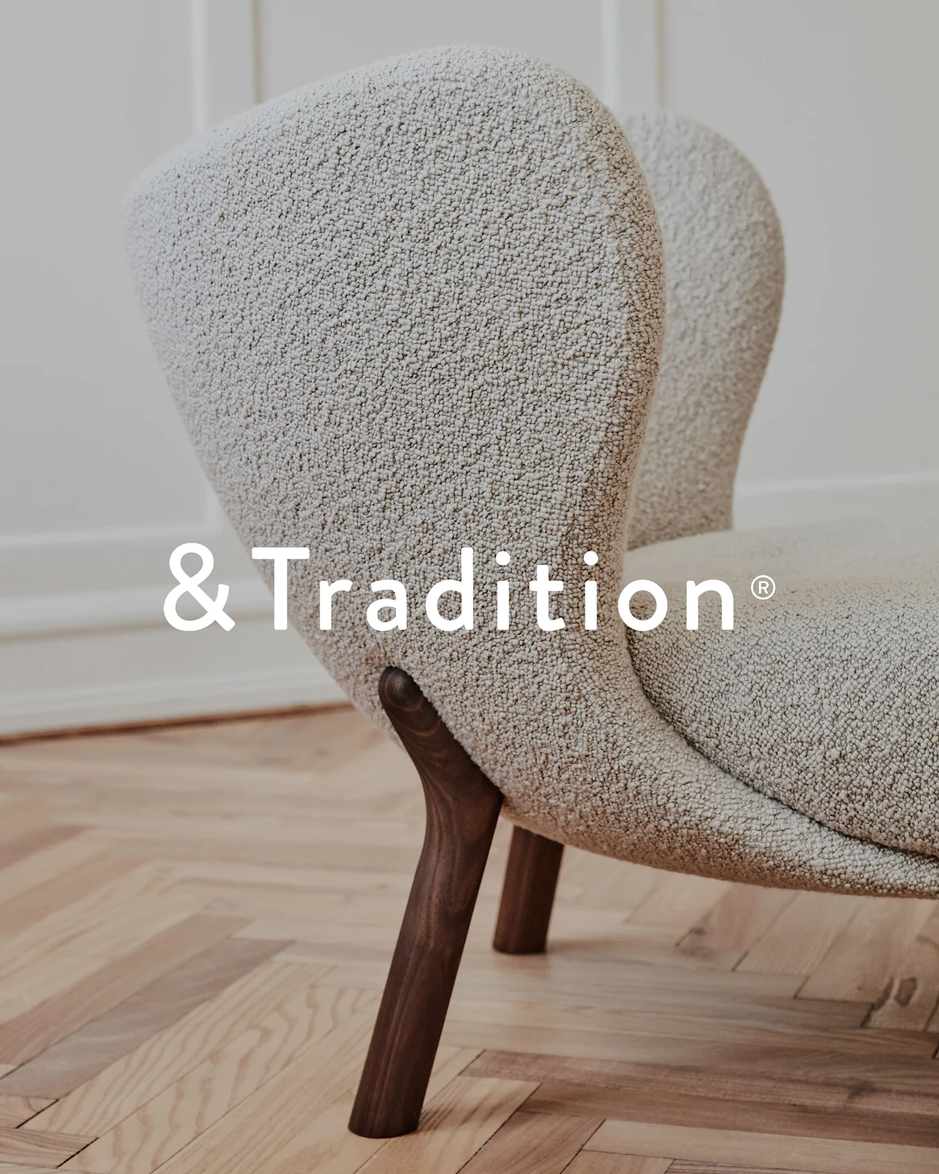 Close-up of a cream textured armchair with dark wooden legs, &Tradition logo.
