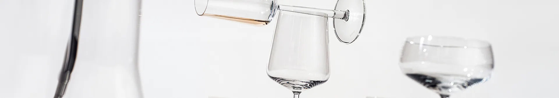 Various clear glass drinkware pieces, including a carafe, champagne flutes, and a wine glass, arranged on a white surface.