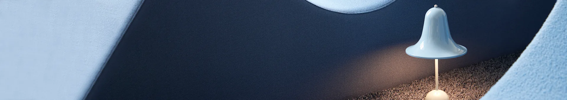 A light blue, bell-shaped lamp illuminates a textured dark gray surface, with dark blue and light blue textured fabrics in the background.