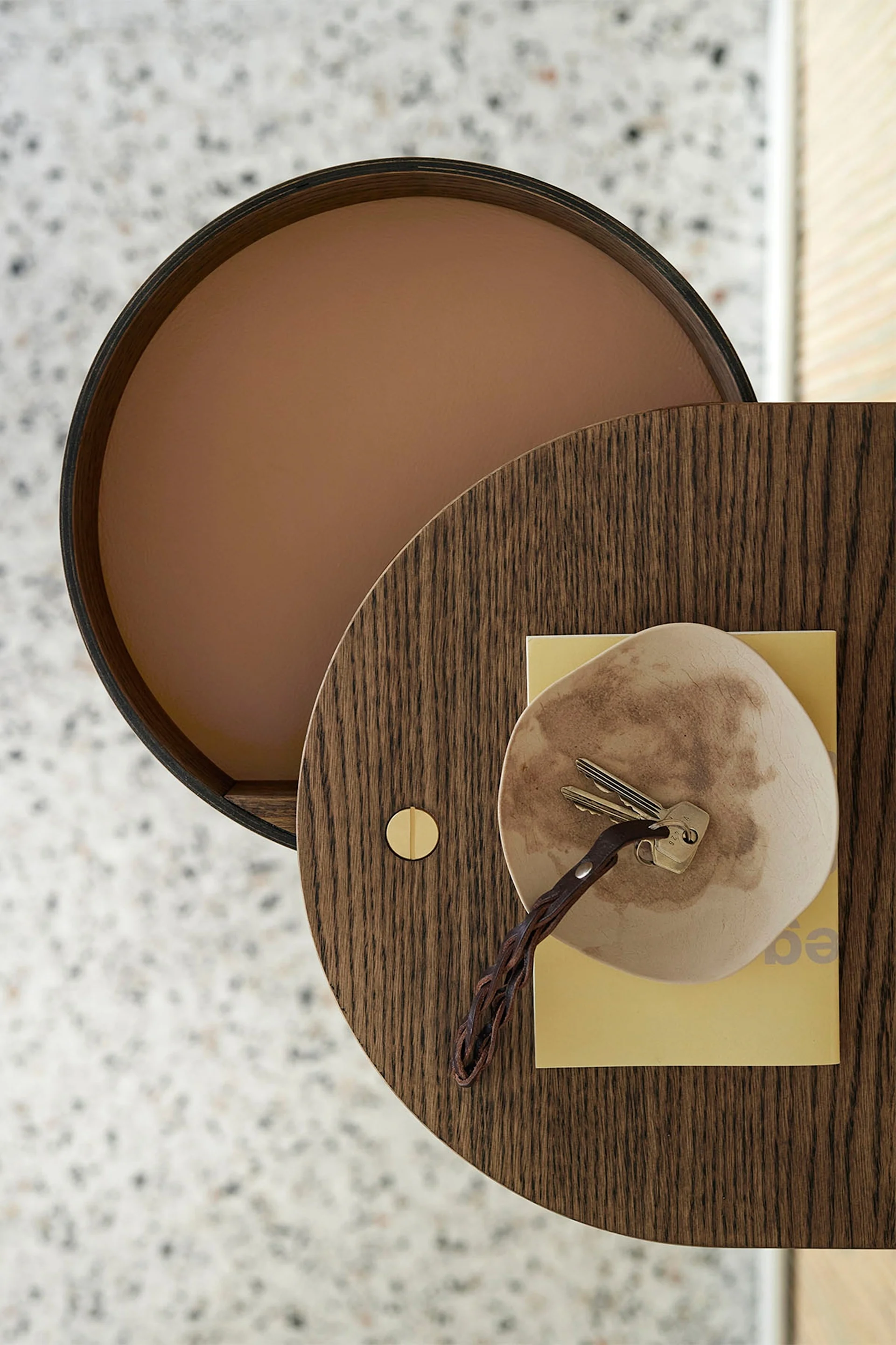 Overhead view of a circular wood table with keys on a dish and a yellow book.