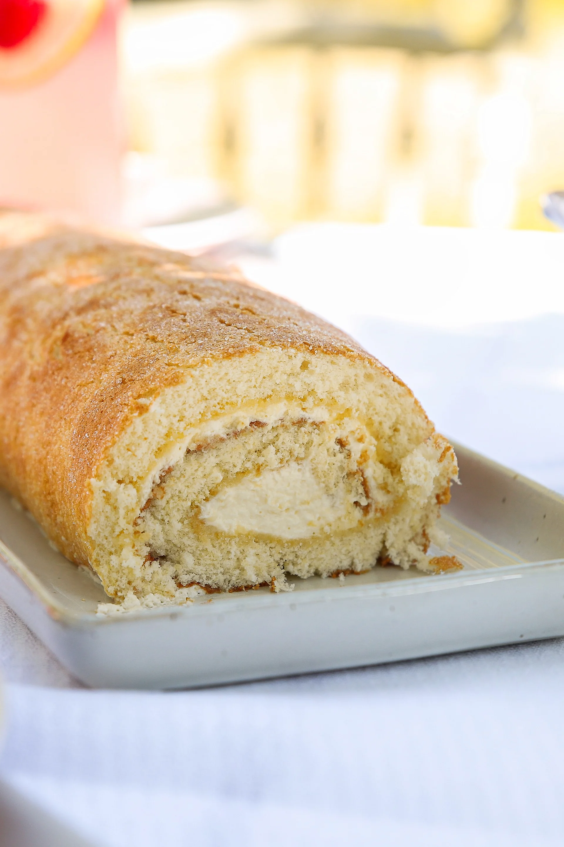 A golden-brown sponge roll with a creamy white filling, sliced on a rectangular platter.