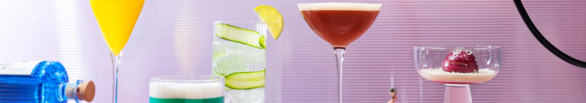 Colorful cocktails and a red dessert in various glasses, with a blue bottle visible.