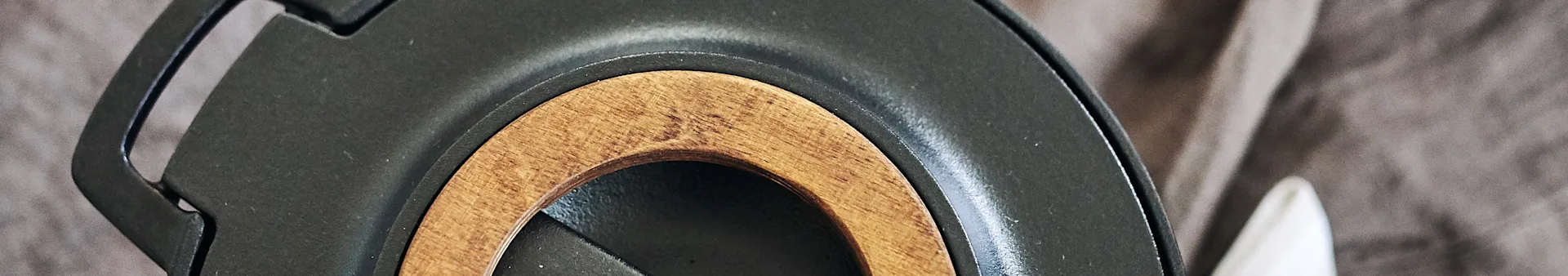 Close-up of a dark gray object with a light brown wooden ring embedded in it, against a blurry fabric background.