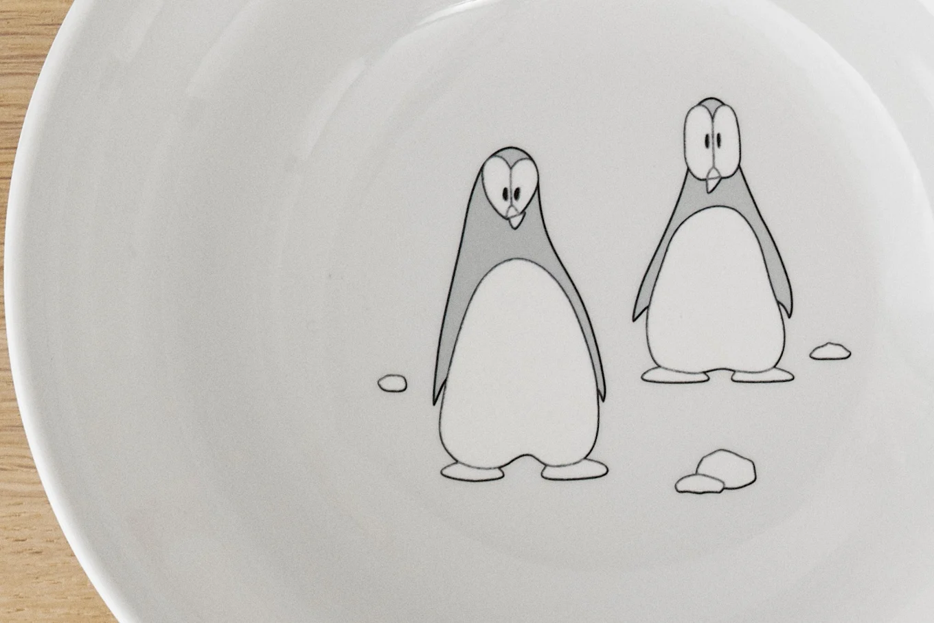 A white plate with two cartoon penguins, one looking down and one looking forward.