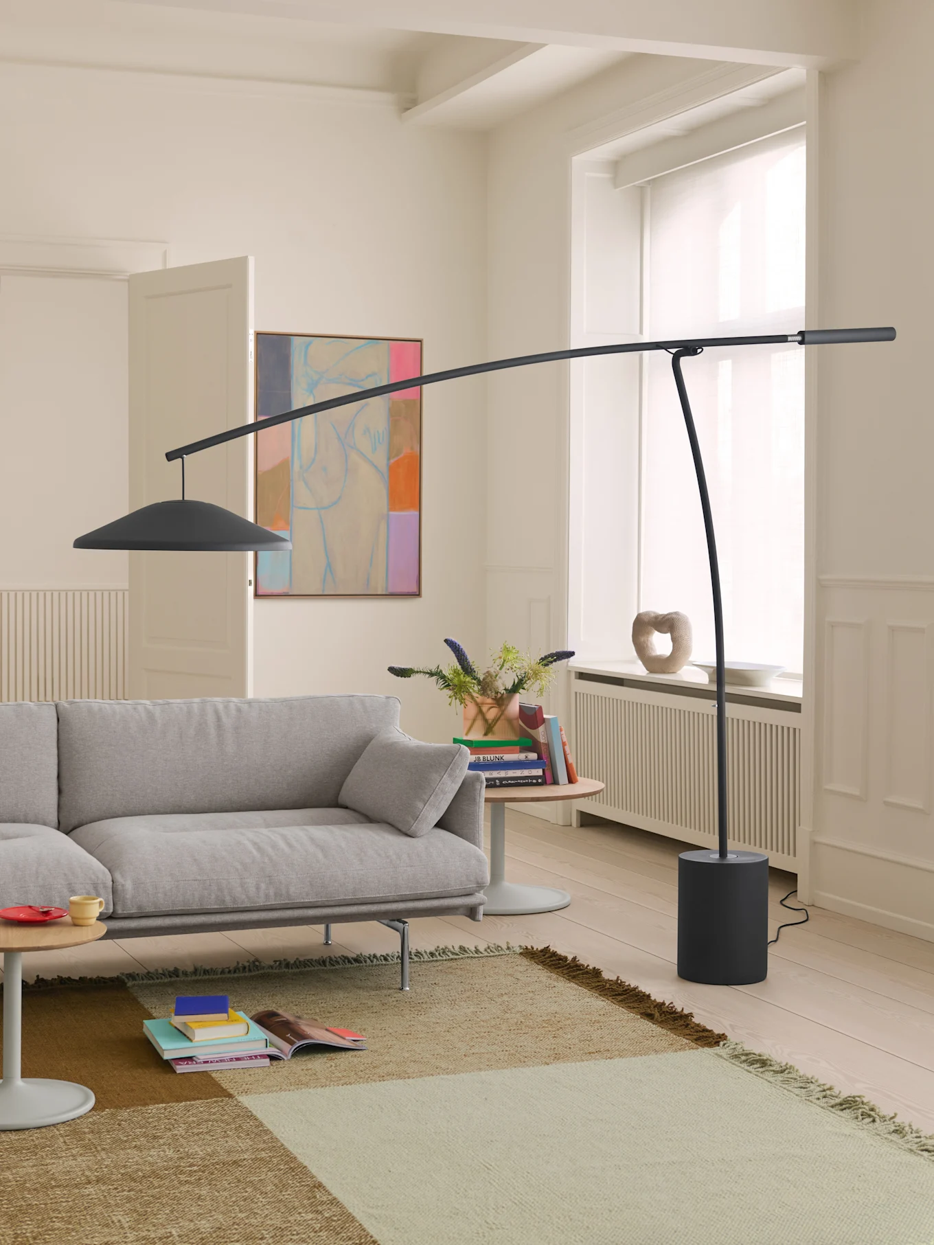 A modern living room with a light grey sofa, a tall dark grey curved floor lamp, and a patterned rug on a light wood floor.