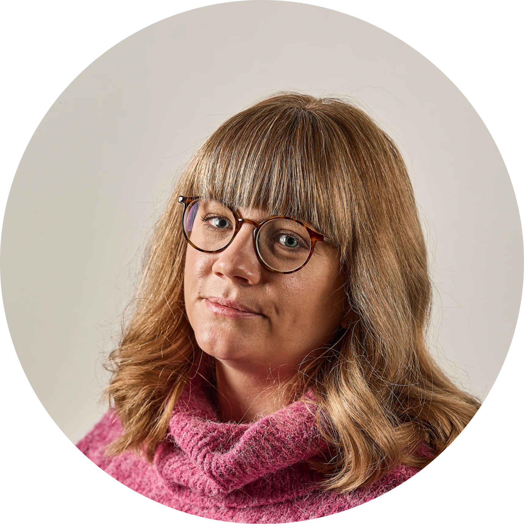 Woman with blonde hair, bangs, and tortoiseshell glasses, wearing a pink turtleneck.