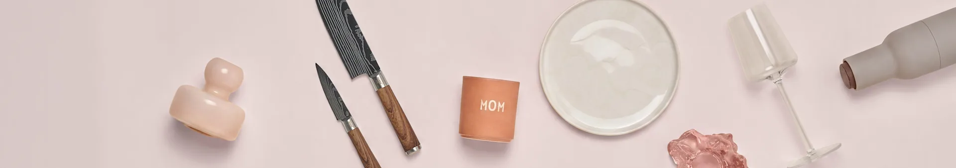 Assortment of kitchenware and decorative items on a pink background, including knives, a plate, a wine glass, and a 'MOM' container.