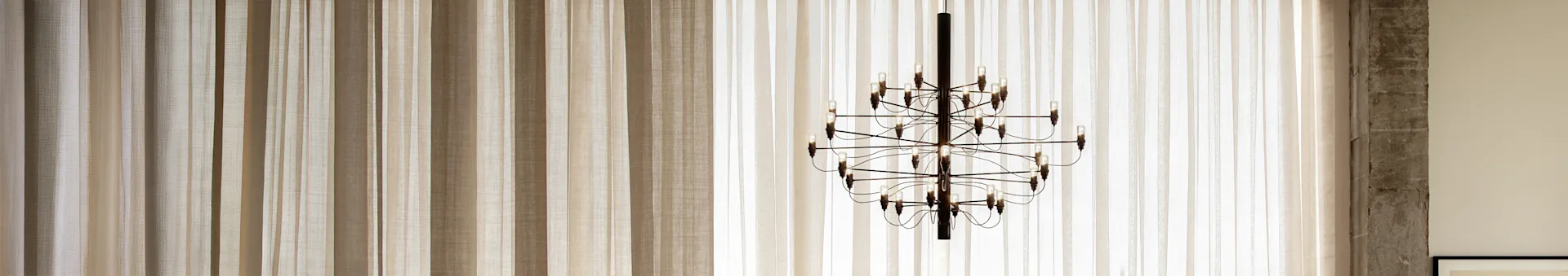 A dark, multi-bulb chandelier hangs in front of light-filtering vertical blinds in varying shades of beige.