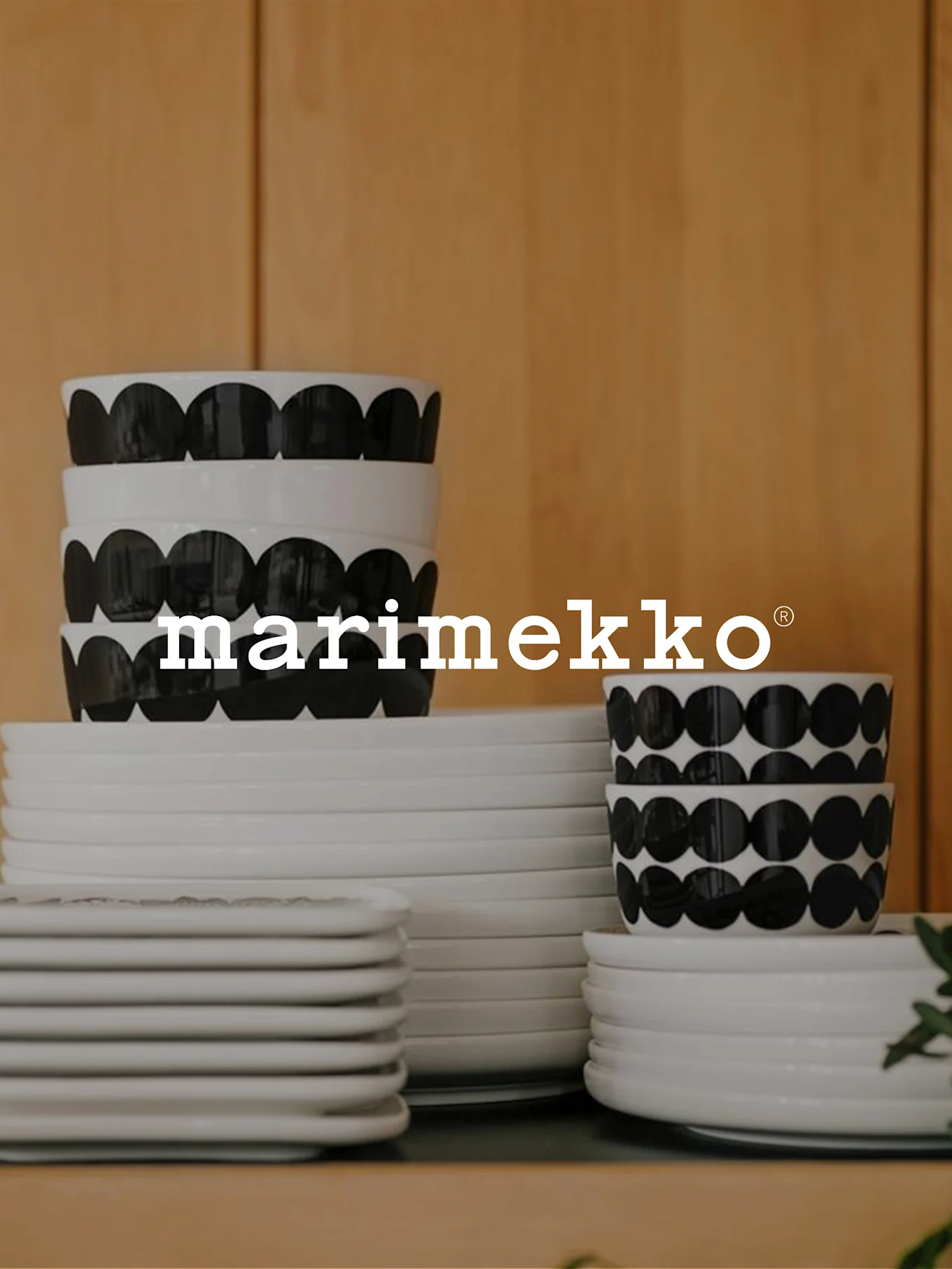 Stacks of white Marimekko plates and bowls with black dot patterns, with the white Marimekko logo overlaid.