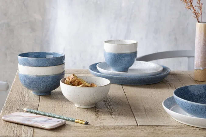 Two-tone blue and white speckled ceramic bowls and plates on a wooden table, with a matching vase.