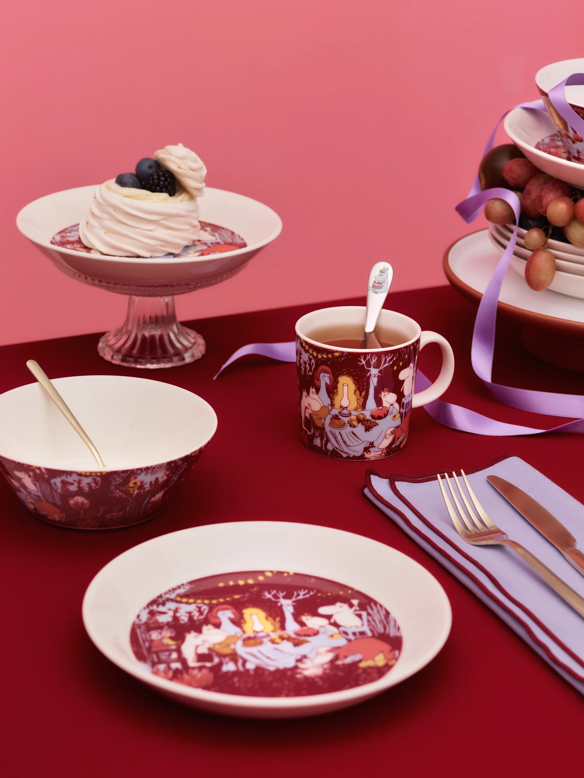 Festive table setting with white dinnerware featuring whimsical red patterns, golden cutlery, a meringue dessert, and a character-themed mug.