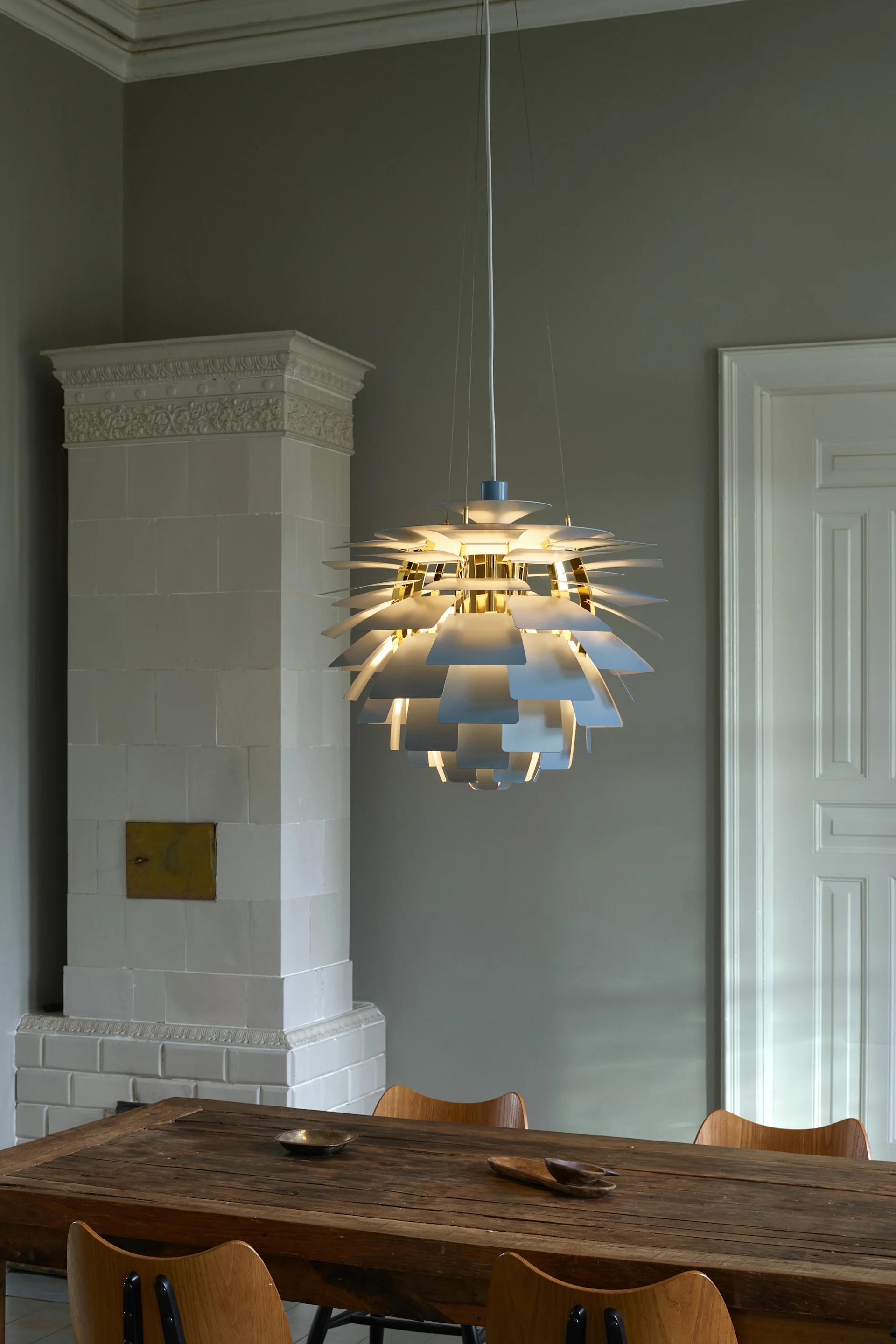 A radiant multi-layered pendant lamp with white and gold accents illuminating a rustic wooden dining table.