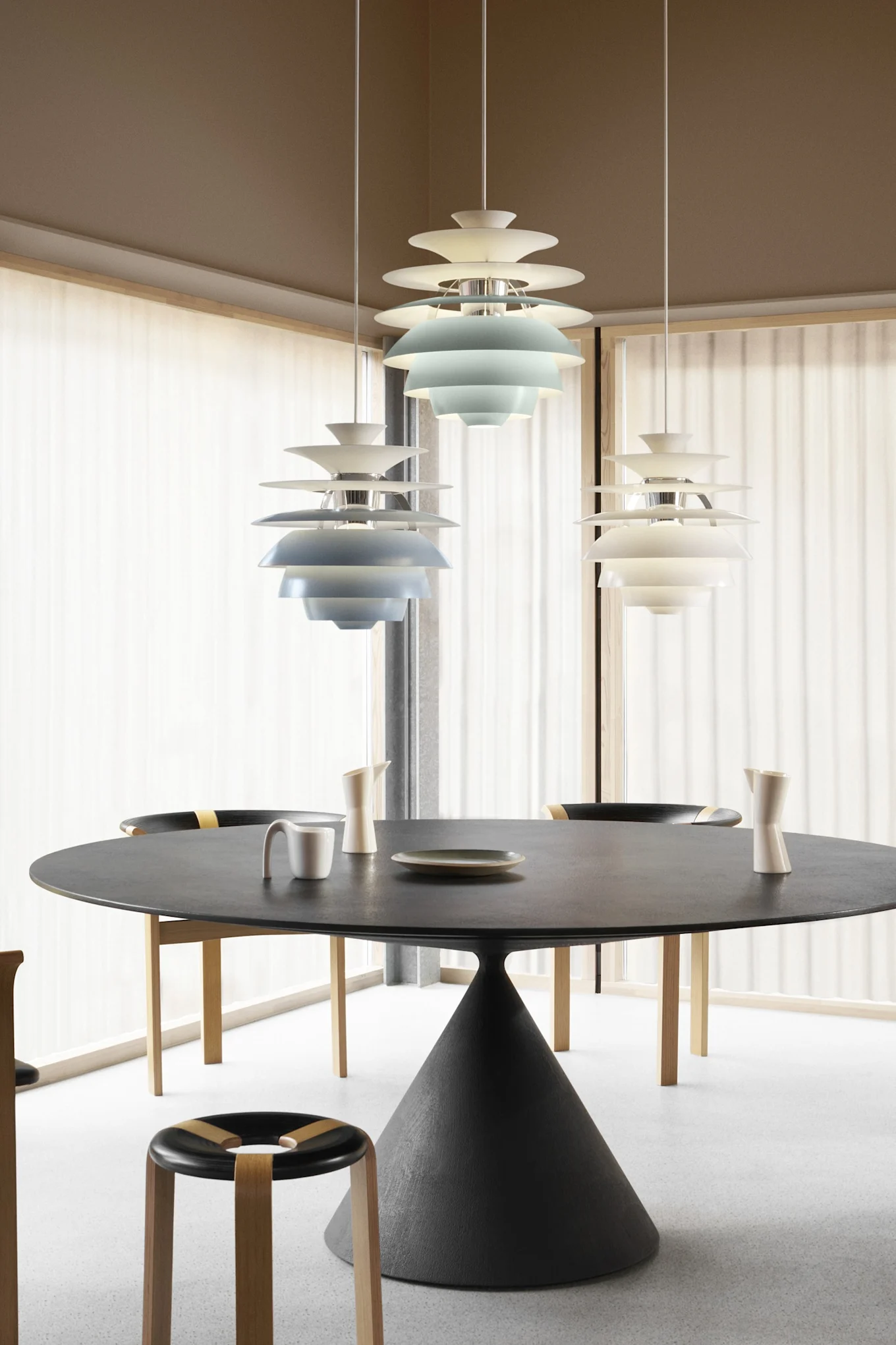 Modern dining room with a round black table, chairs, and three tiered pendant lights, two blue and one white.