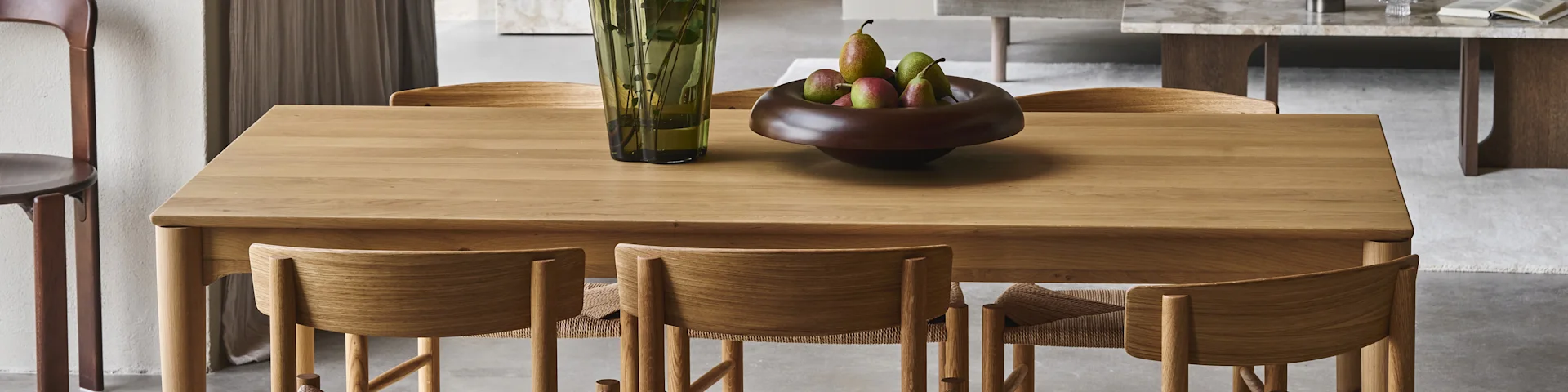 A wooden dining table with matching chairs, a green vase, and a bowl of pears.