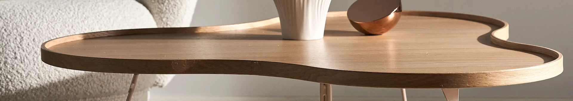 Close-up of a wooden, wavy-edged side table with a white vase and a copper decorative object.
