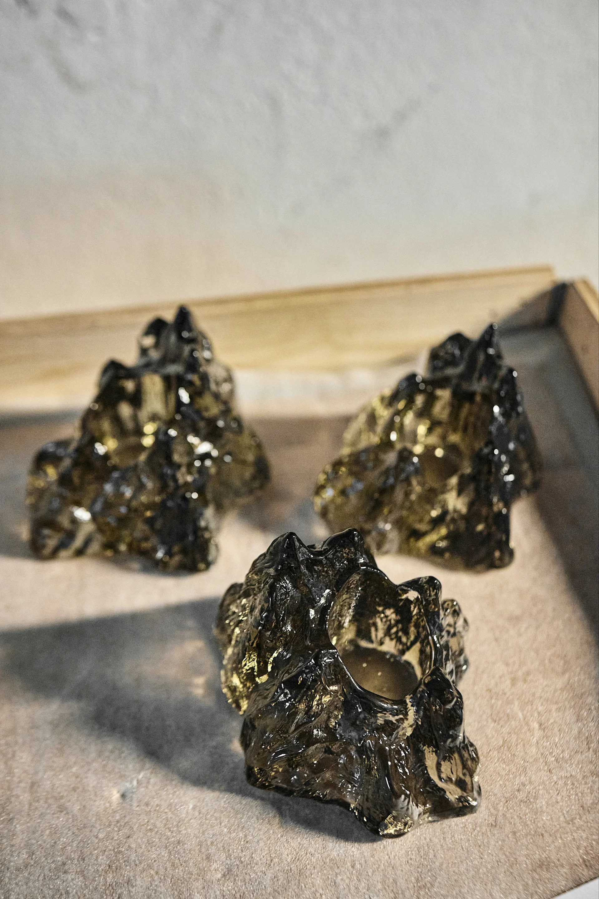 Three dark, irregularly shaped translucent glass candle holders on a light brown surface.