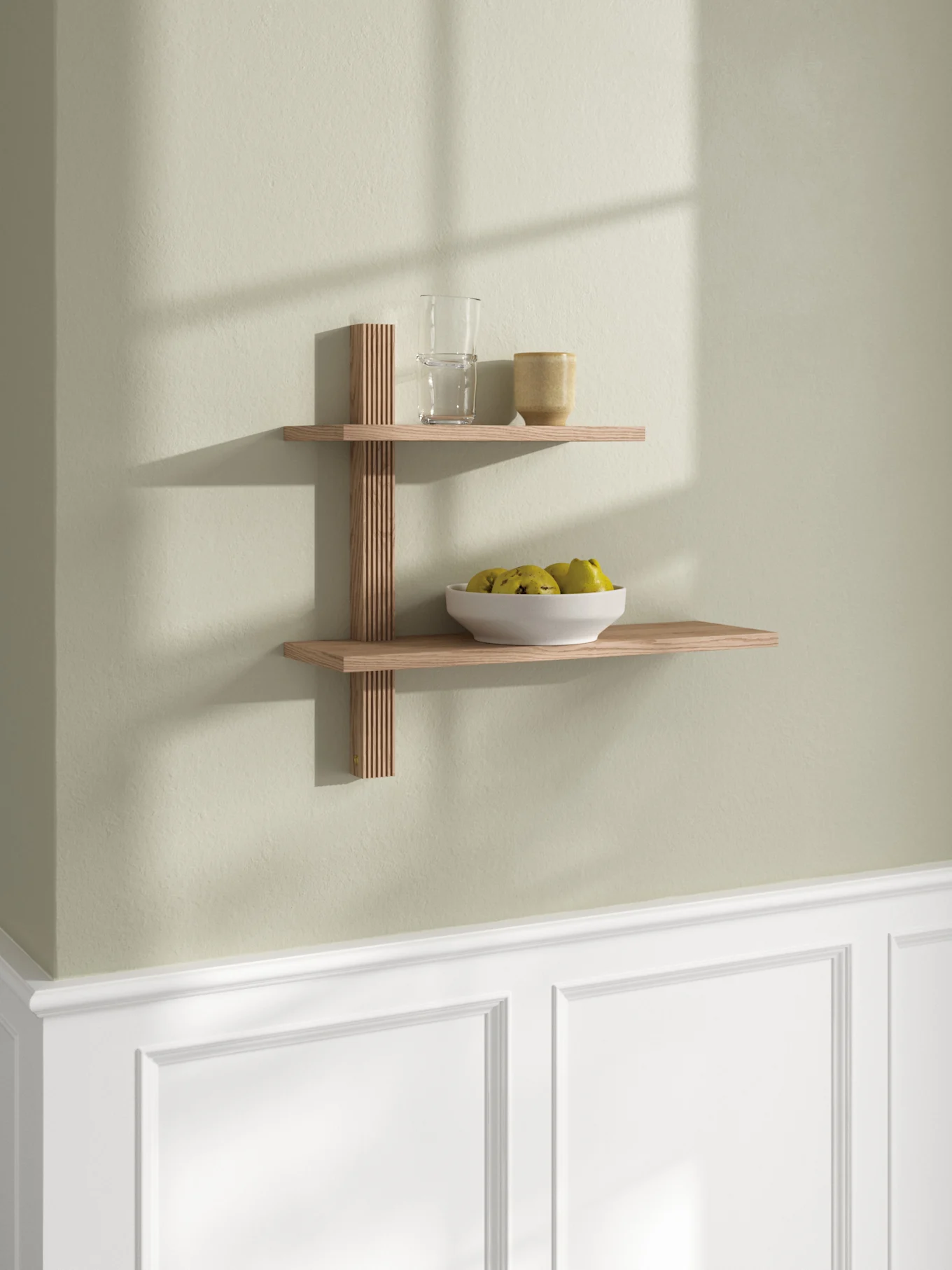 Two-tier wooden wall shelf with slatted support, holding a glass, a mug, and a bowl of yellow-green fruit.