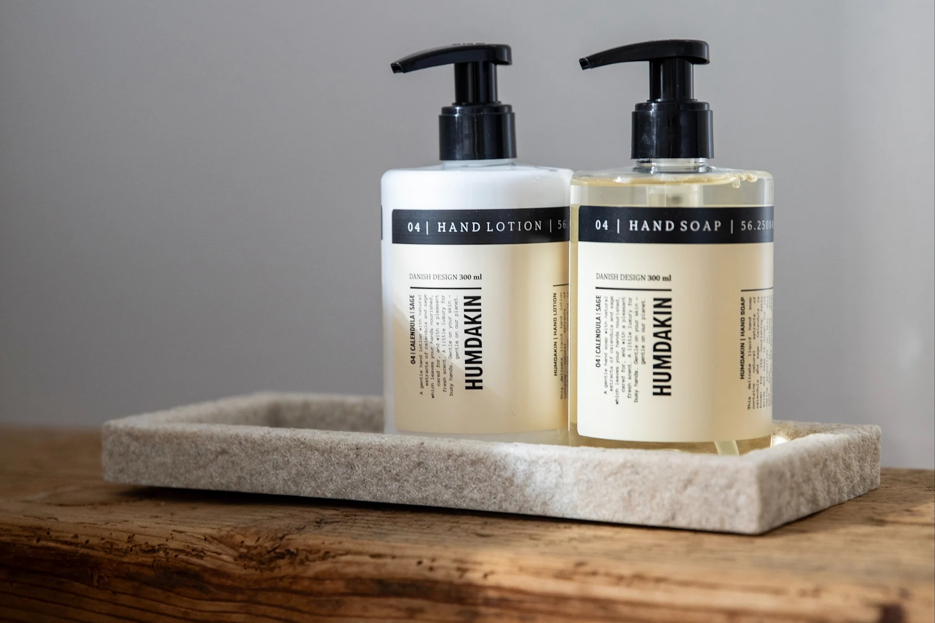 Two Humdakin pump bottles, hand lotion (white) and hand soap (clear), on a stone-like tray on wood.