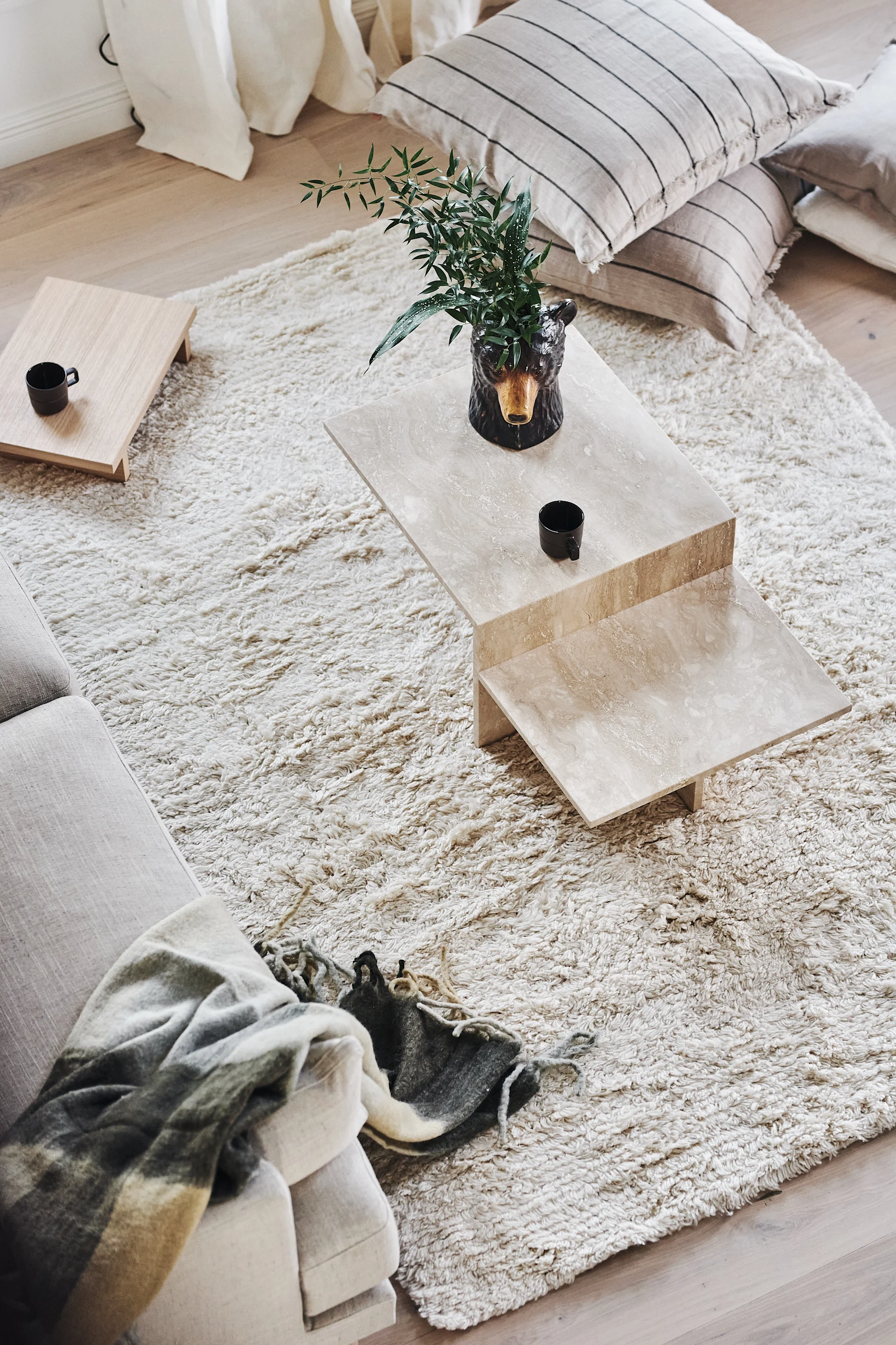 Overhead view of a living room with a shaggy rug, travertine coffee table with bear vase, sofa with plaid throw, and striped cushions.