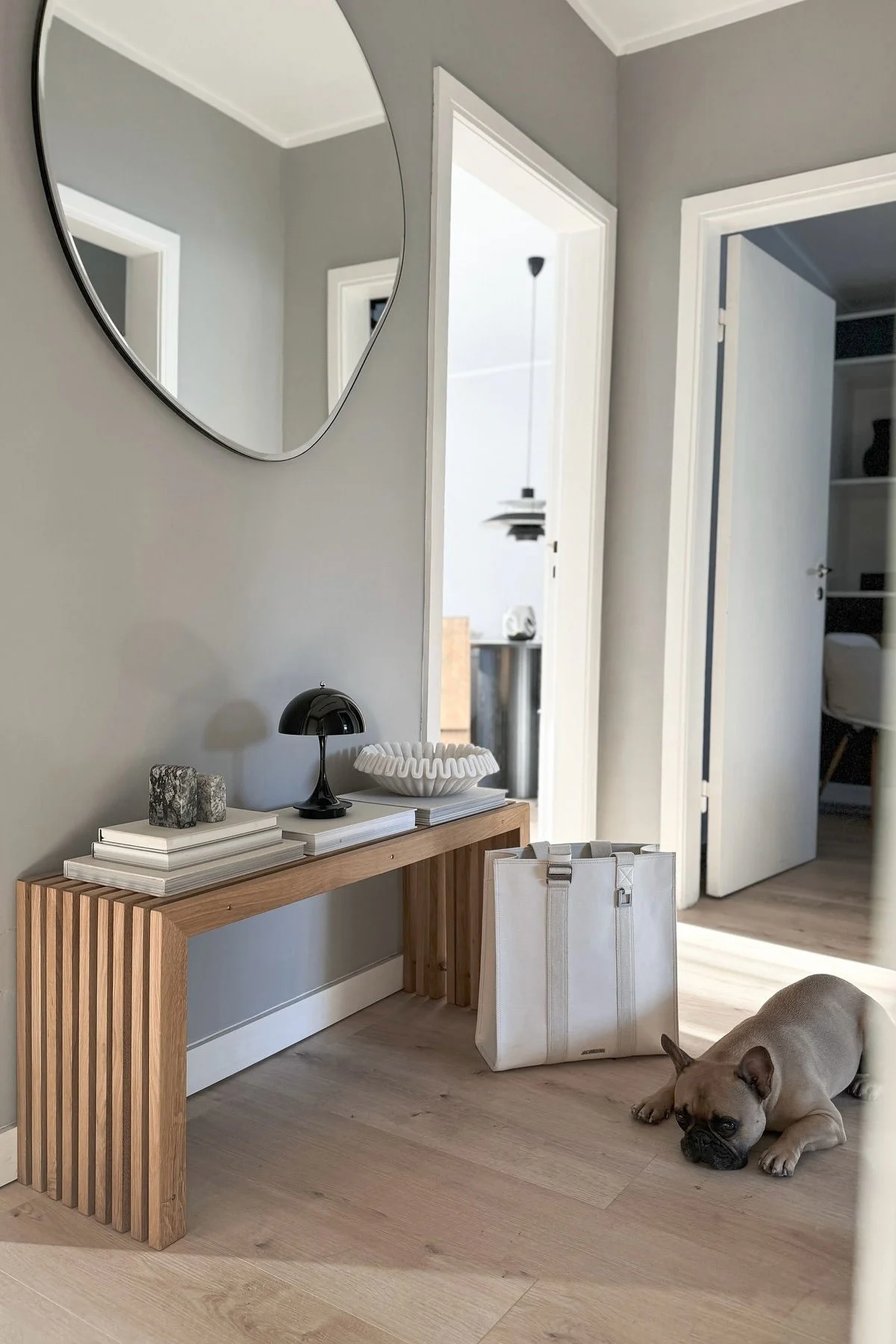 A modern hallway with a wooden console table, decorative items, and a French Bulldog on the floor.