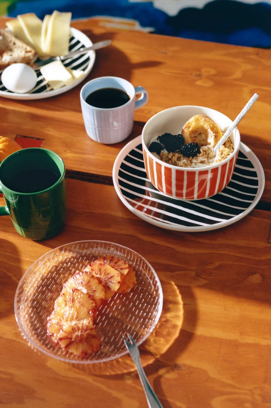 Breakfast on a wooden table with striped dishes, coffee, oatmeal, cheese, bread, egg, and blood orange slices.