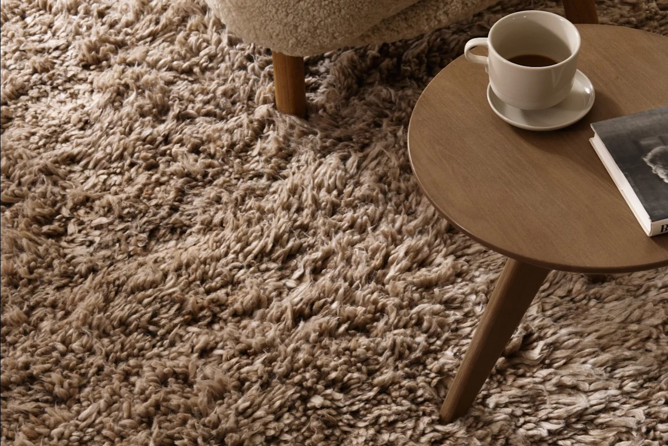 Overhead view of a shaggy brown rug with a wooden side table holding a coffee cup and a book.