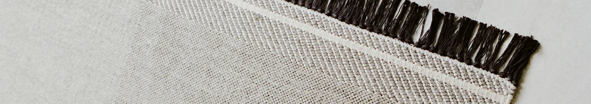 Woven rug with off-white and brown textured pattern and dark fringes.