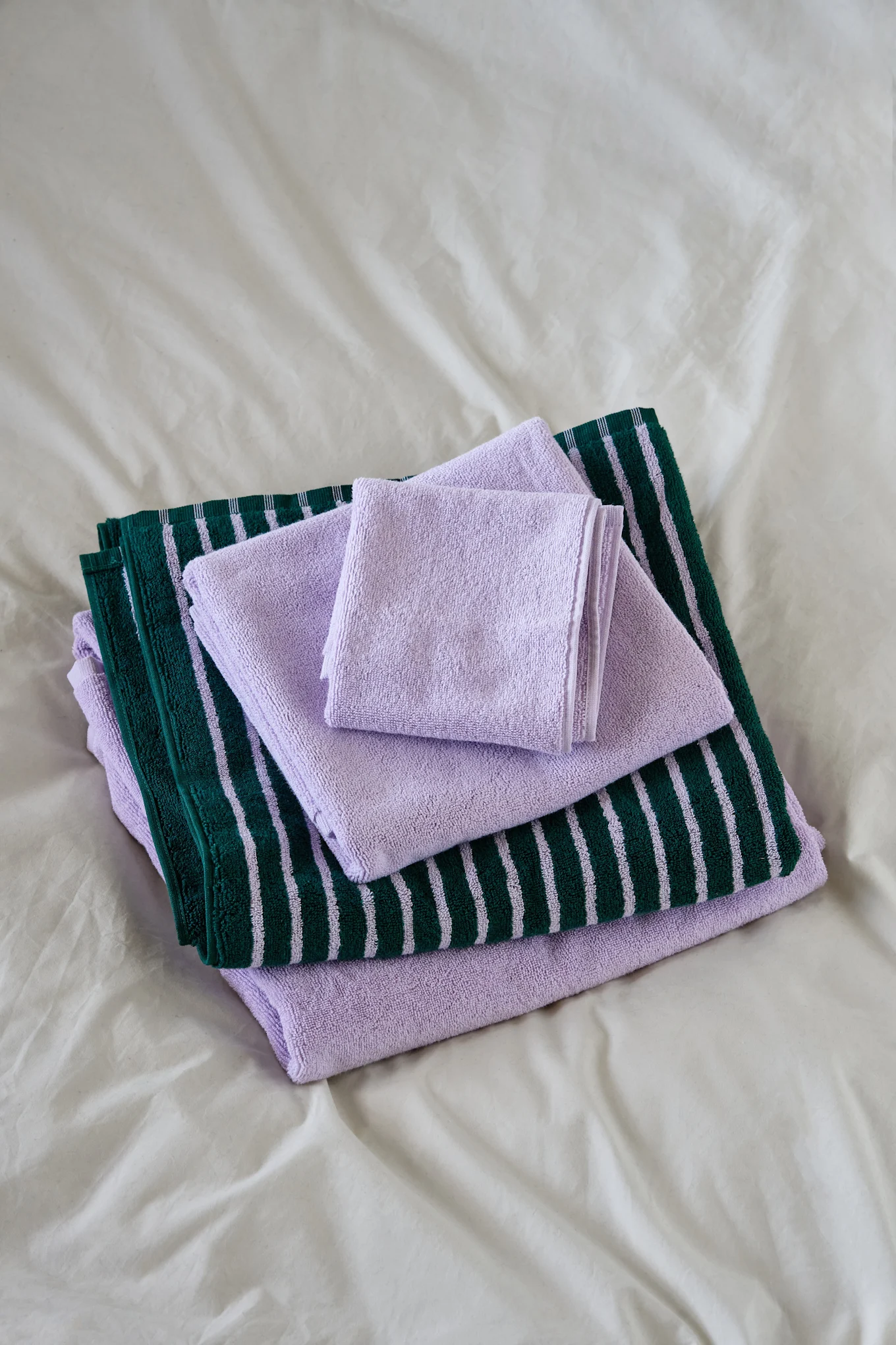 Stacked folded towels: light purple, and dark green with light purple stripes, on a white sheet.
