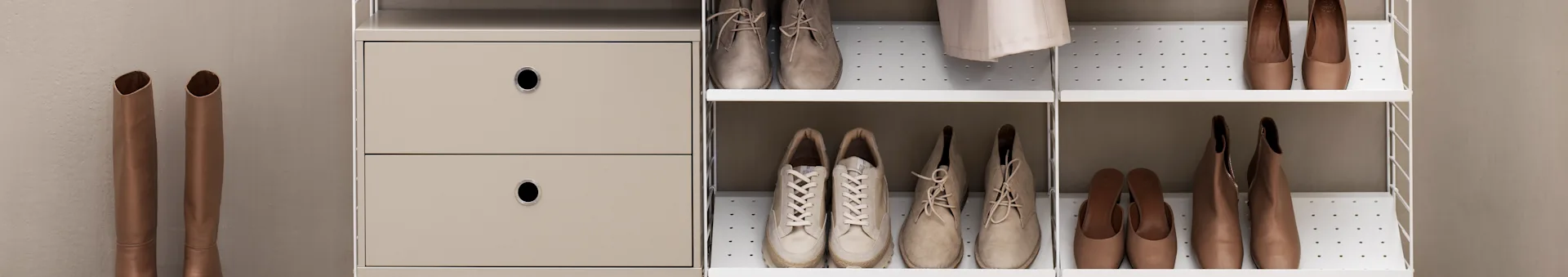 Various pairs of light brown and beige shoes on white shelves next to modular drawers and tall boots.