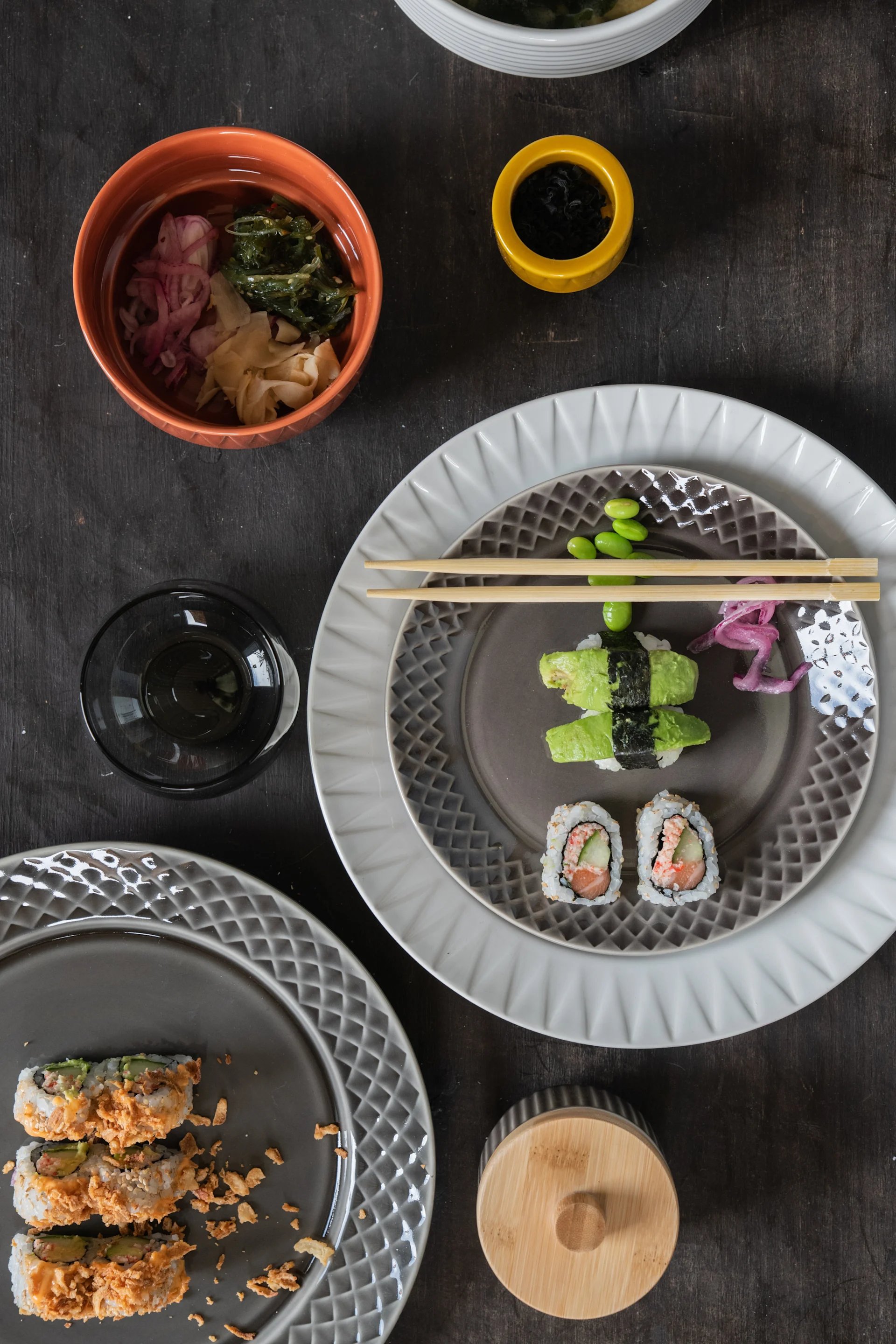 Overhead view of a sushi spread: avocado nigiri, salmon maki, and crispy fried sushi, with seaweed salad, pickled ginger, and edamame.