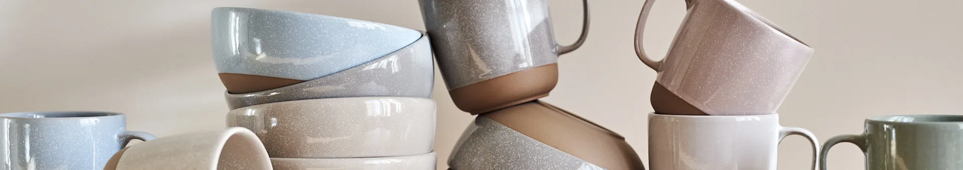 Stacked ceramic bowls and mugs in various speckled pastel colors.