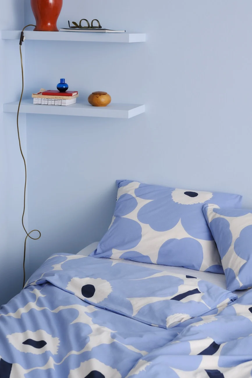 A bedroom corner with light blue walls, two floating shelves, and a bed with blue and white floral bedding.