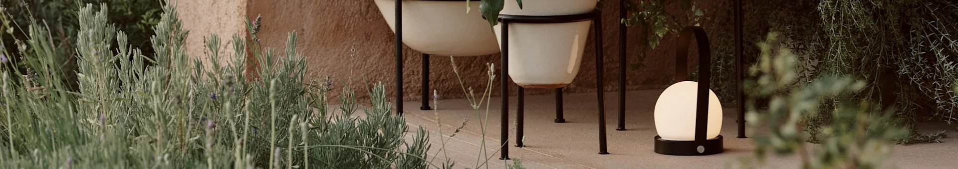 Outdoor scene with two light-colored planters on black stands, a glowing spherical lamp with a black handle, and lush lavender plants.