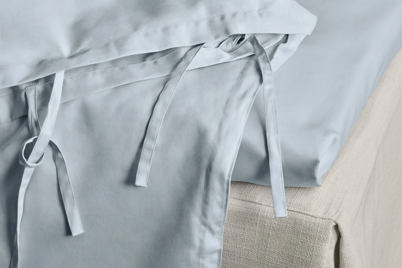 Detail of light blue duvet cover with fabric ties, on a textured beige bed.