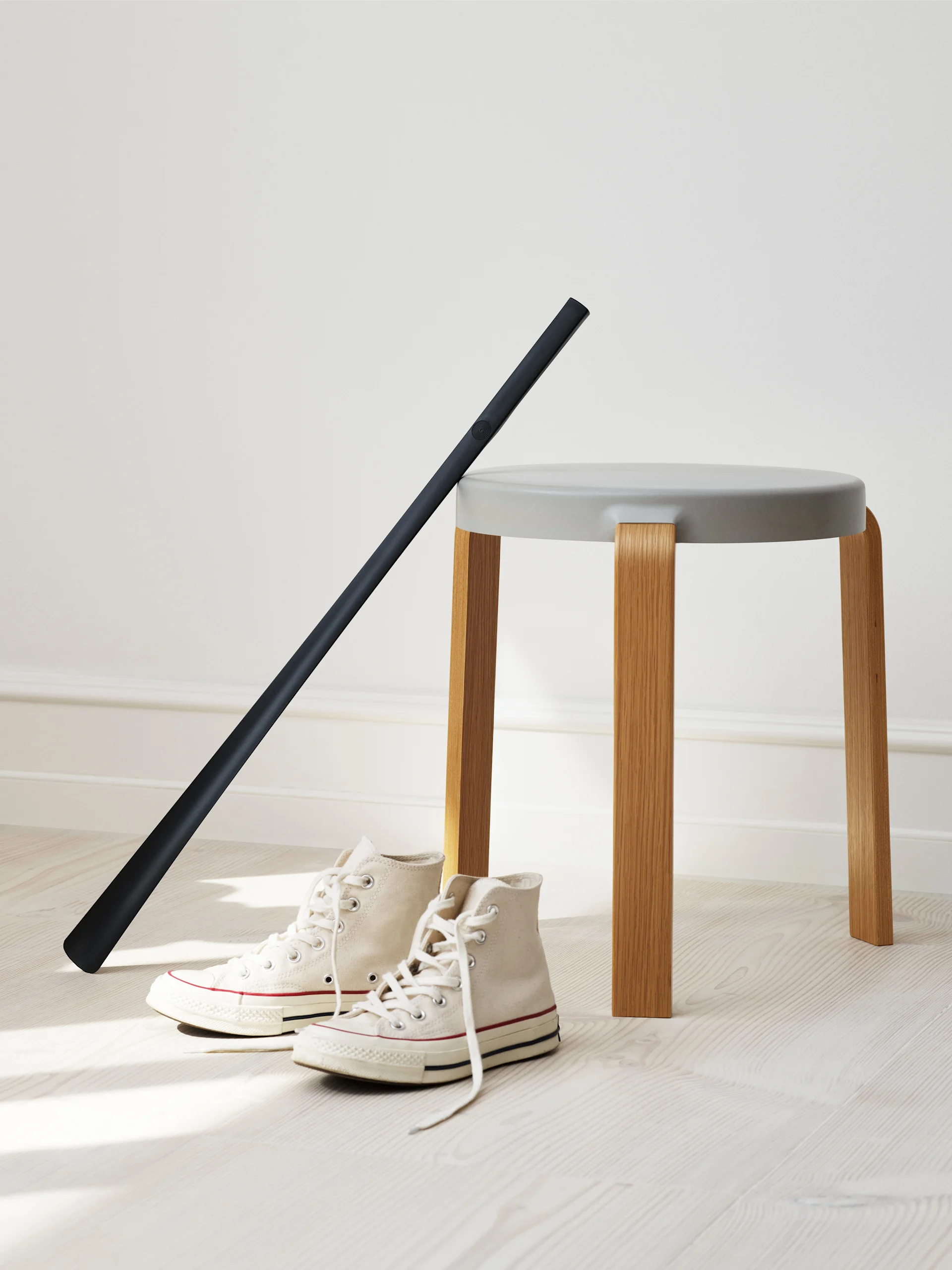 Off-white high-top sneakers, a dark grey shoehorn, and a light grey stool on a light wooden floor.