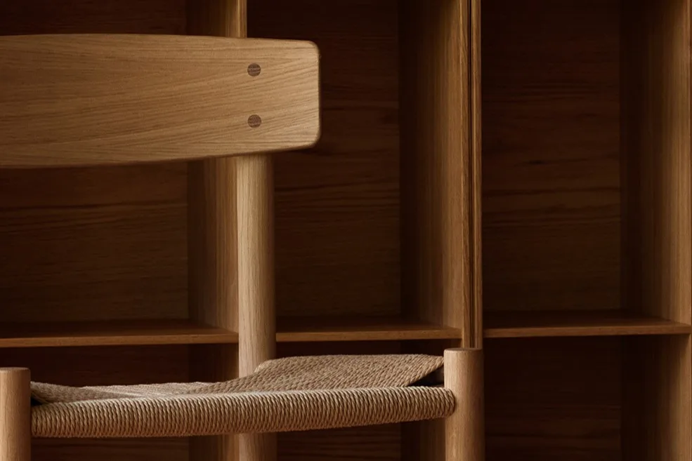 A light wood chair with a woven seat against a wall of square wooden shelves and a patterned wood floor.