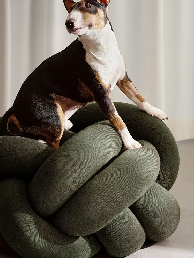 Tricolor Bull Terrier dog sitting on a dark green knotted cushion, looking right.