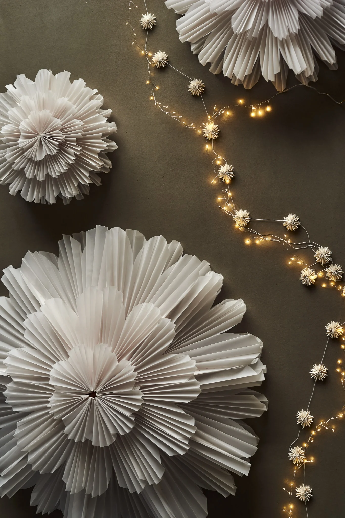White pleated paper decorations and string lights with paper stars on a dark background.