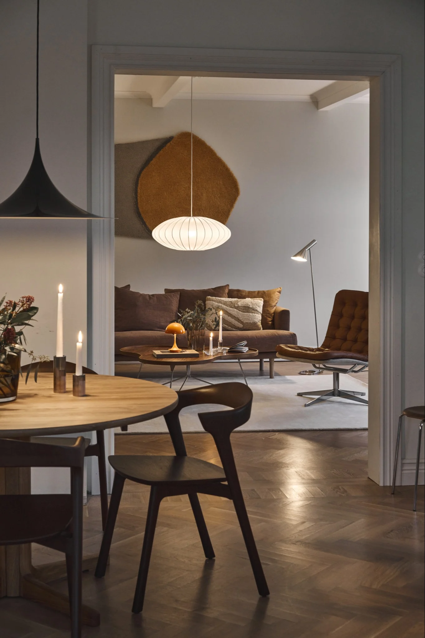 View from a dining room into a modern living room with various lamps, a brown sofa, and a leather lounge chair.
