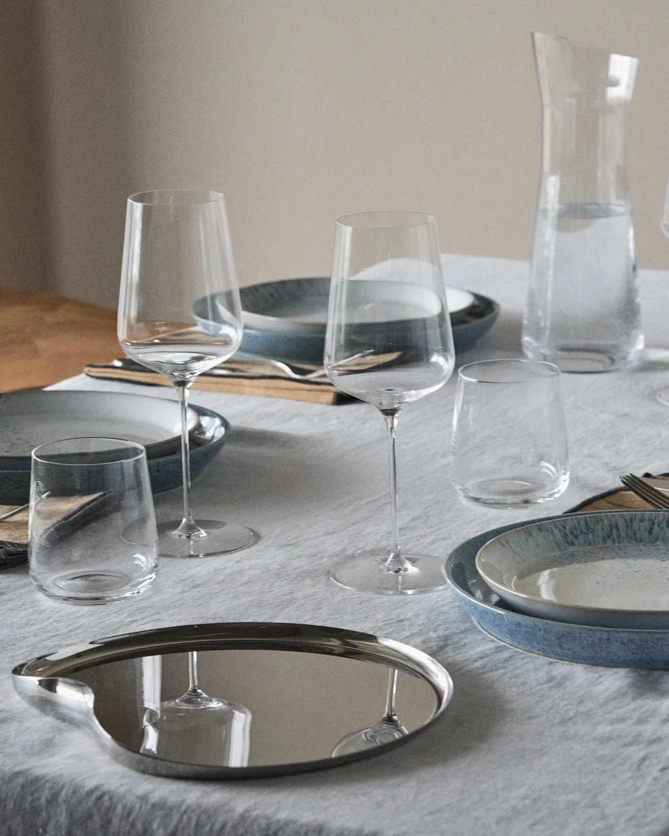 Table set with blue and speckled plates, wine glasses, tumblers, a water carafe, and a reflective oval tray.
