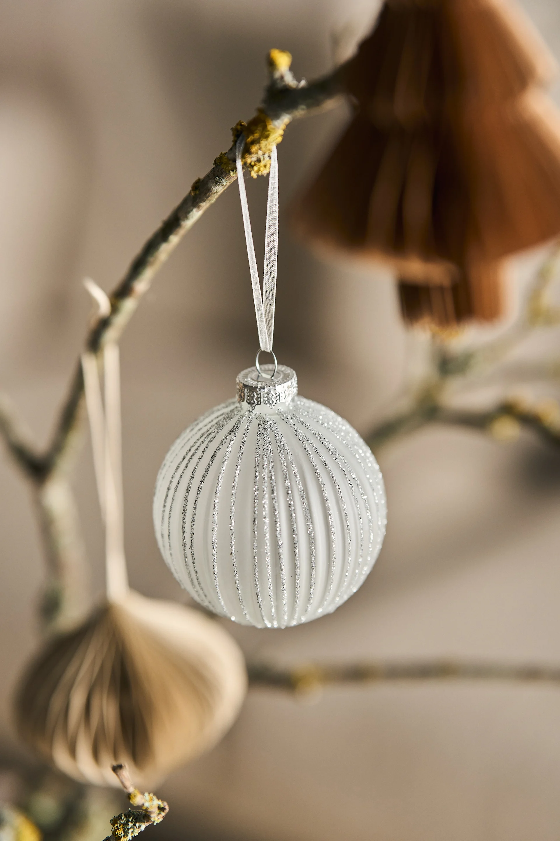 White Christmas ornament with vertical silver glitter stripes hanging from a branch.