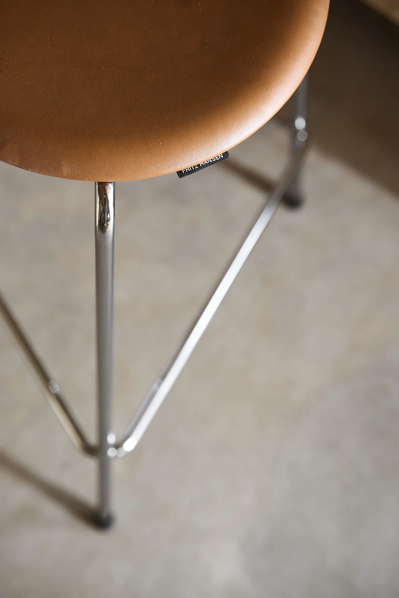 Close-up of a brown leather stool seat with chrome legs and a 'Fritz Hansen' label.