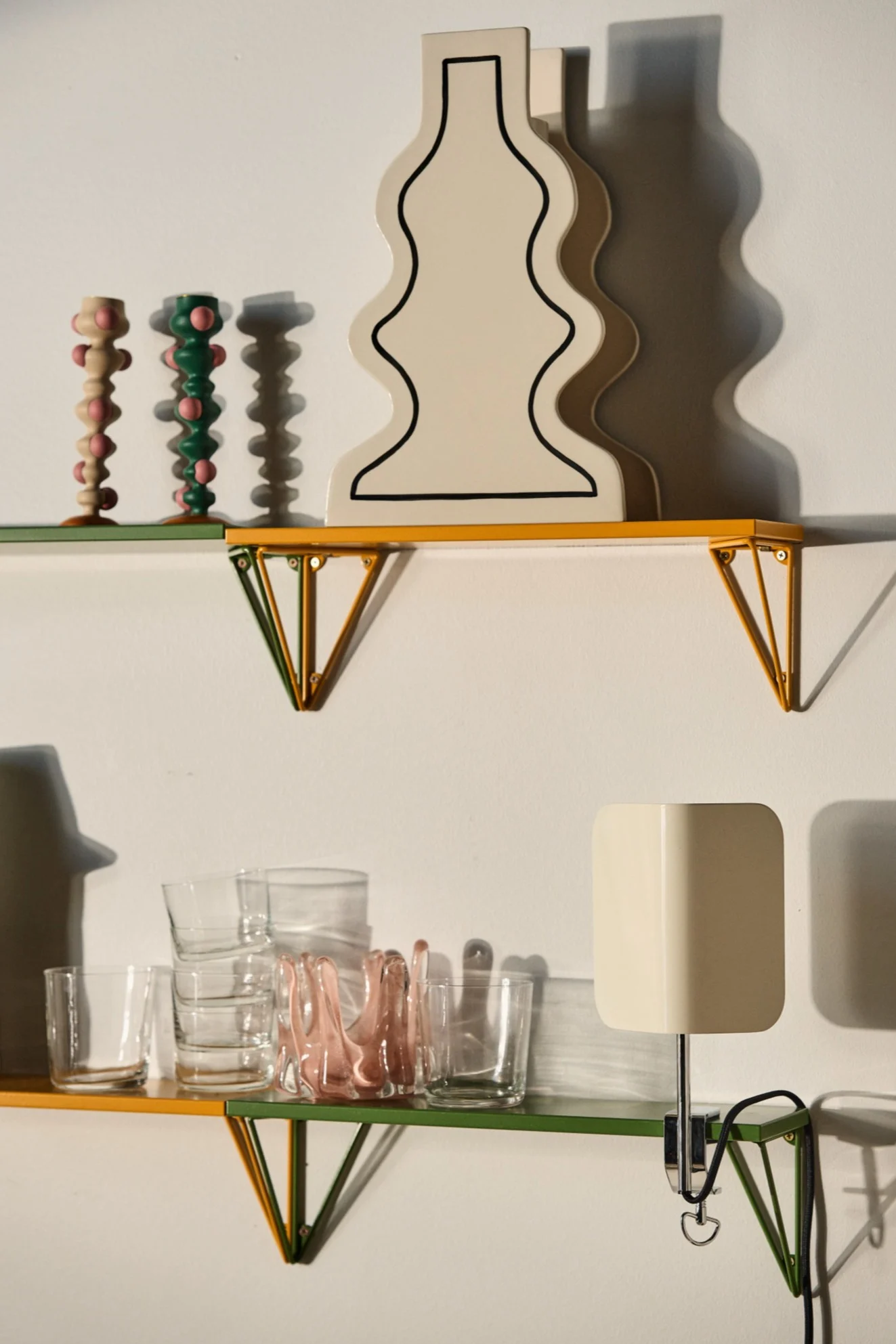 The Pythagoras shelf from Maze in contrasting colours of yellow and green with a collection of glasses, candle holders and vases.