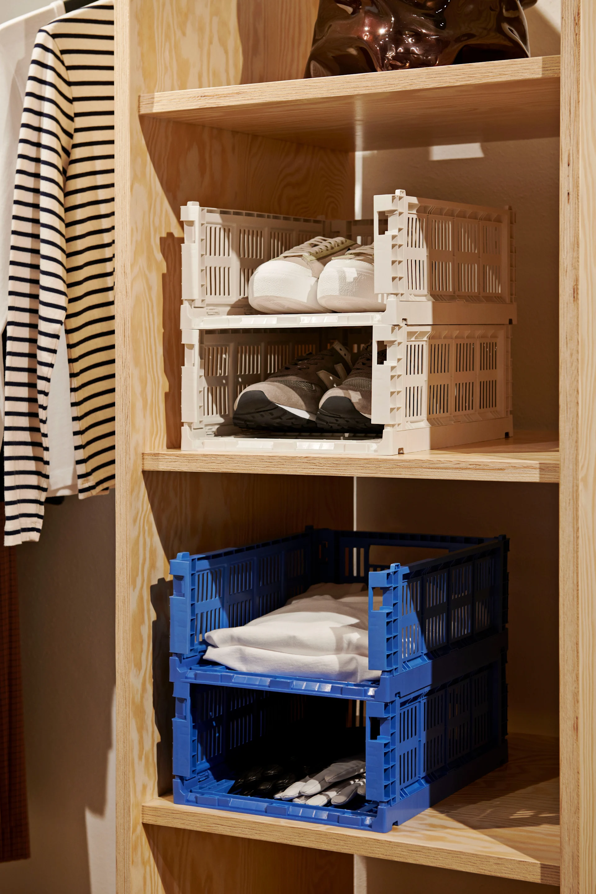 Wooden shelves, a striped shirt, sneakers in stacked beige crates, folded items in stacked blue crates.