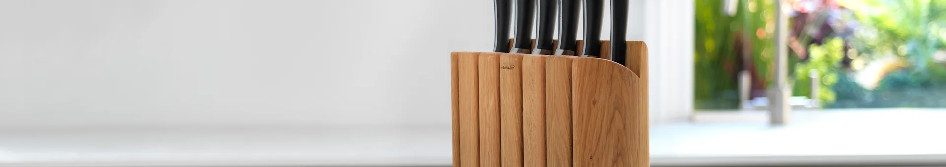 Wooden knife block holding several black-handled kitchen knives.