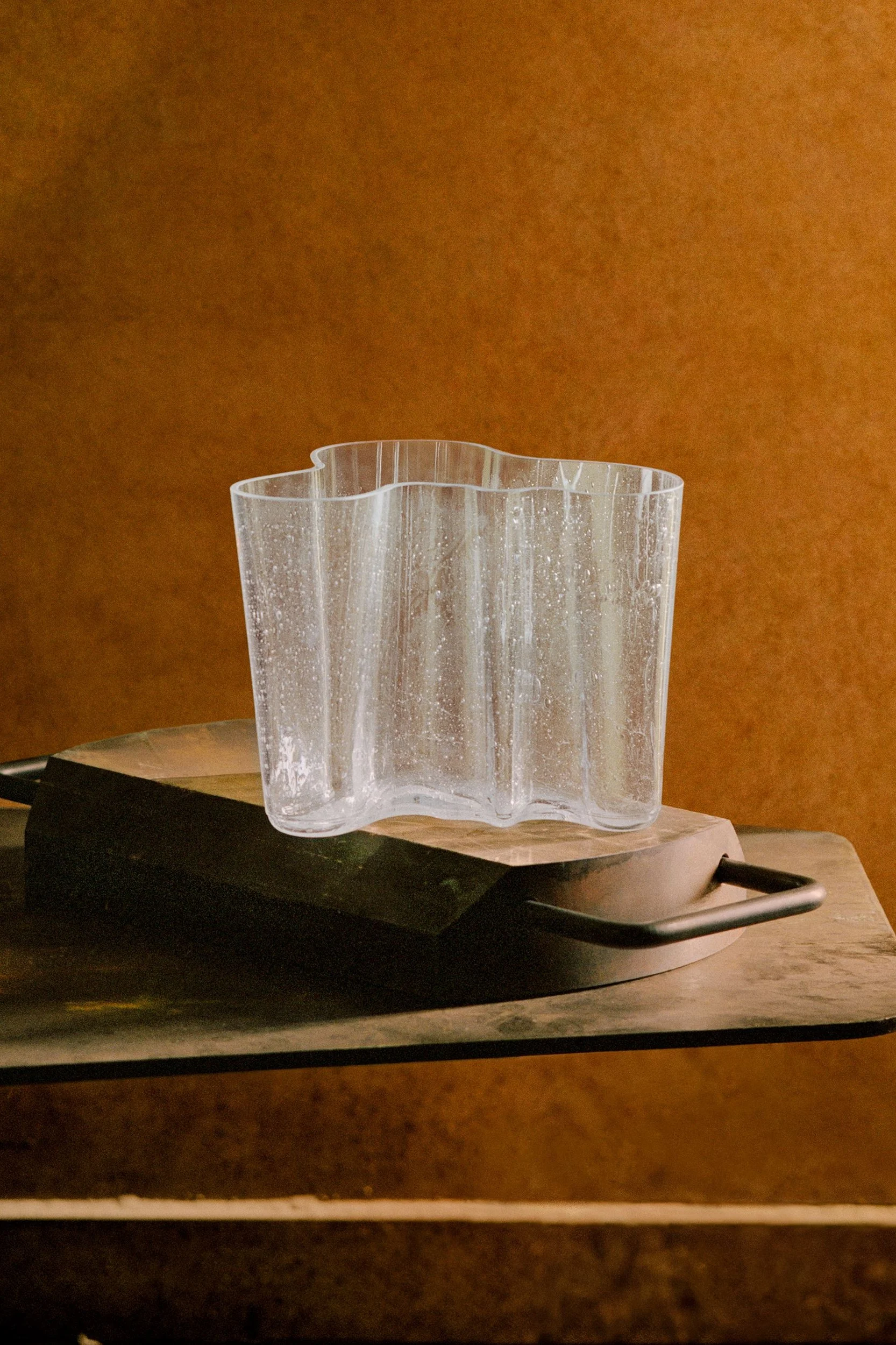 Clear wavy glass vase with a textured surface on a wooden board.