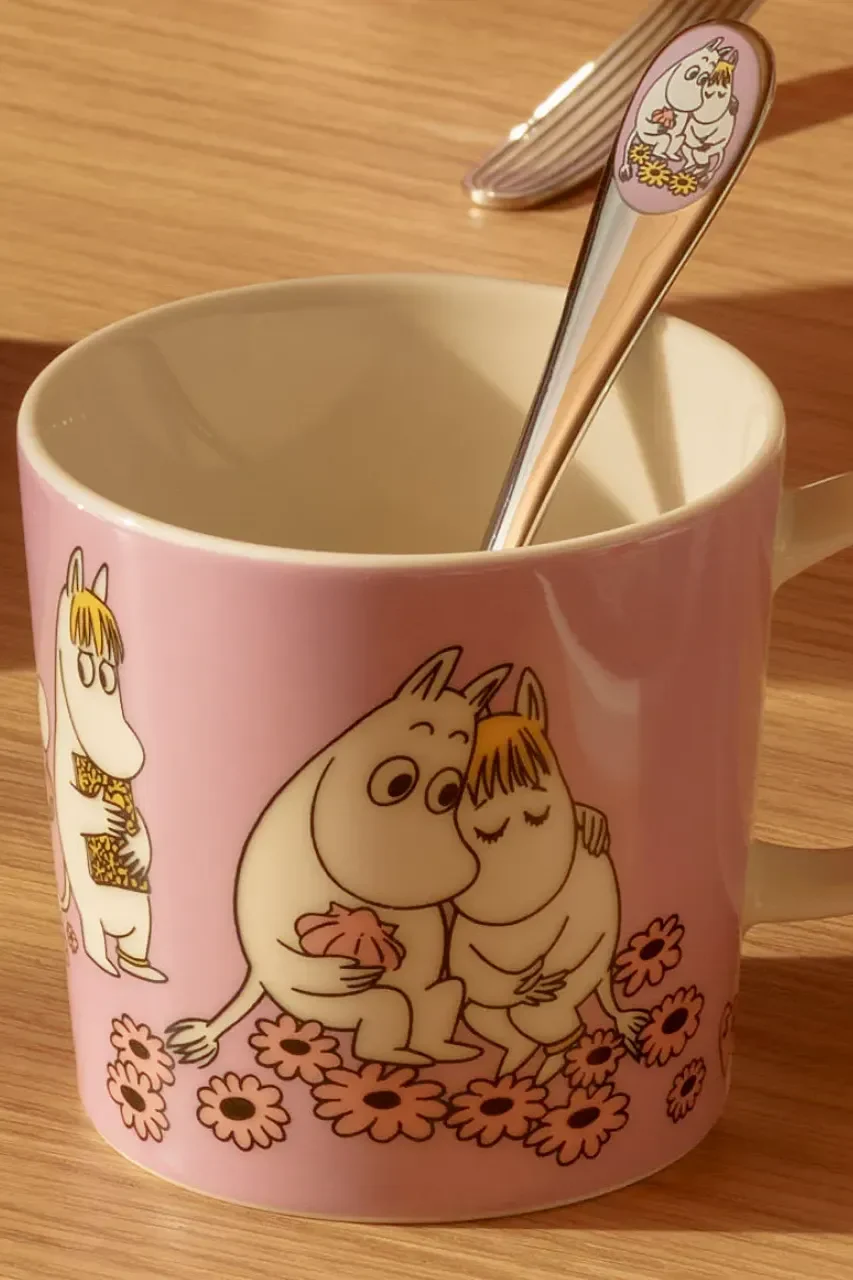 Pink Moomin mug with Moomintroll and Snorkmaiden hugging among flowers, and a Moomin spoon inside.