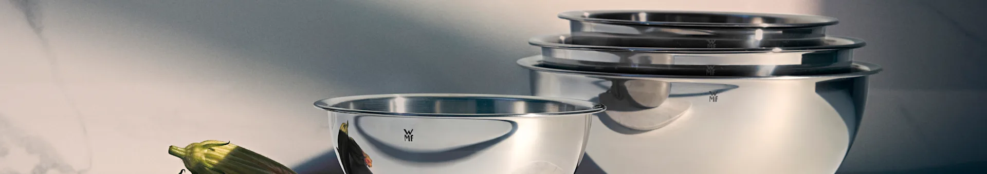 Shiny WMF stainless steel mixing bowls, one in foreground, others stacked, with a green vegetable.