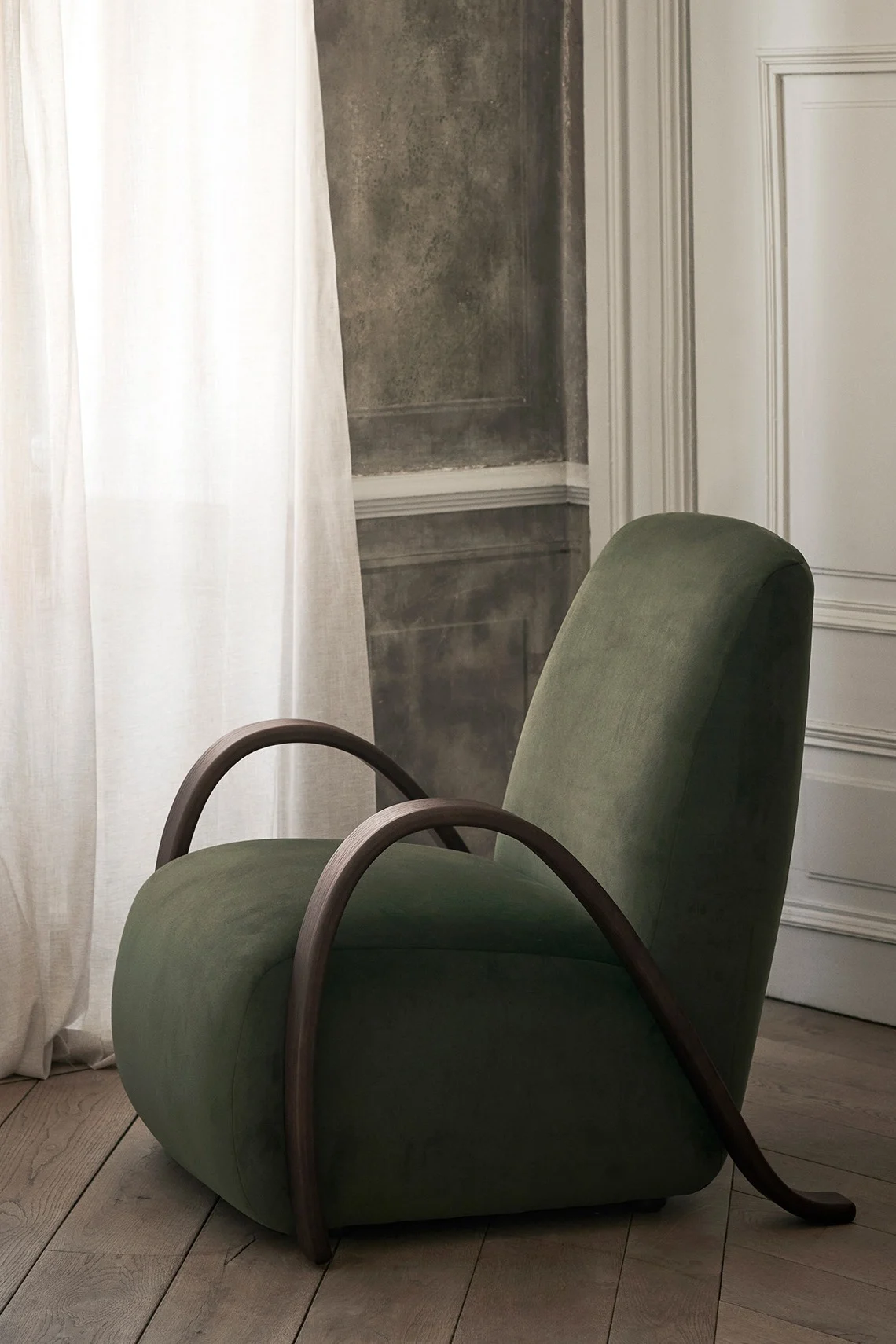 Dark green velvet armchair with curved wooden frame in an elegant room.